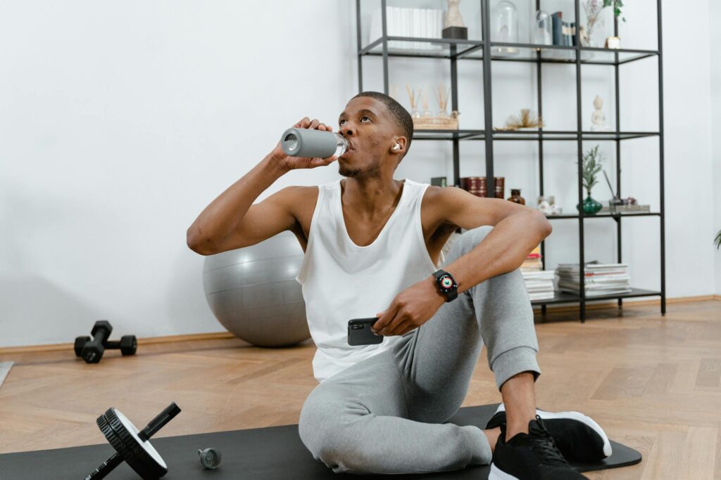 A man in a home gym setting drinks water post workout, showcasing fitness.