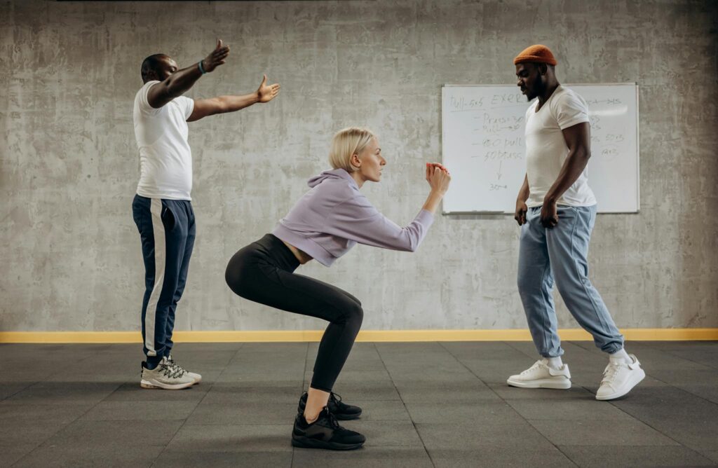 Three diverse adults engaged in a fitness class, focusing on squatting techniques indoors.