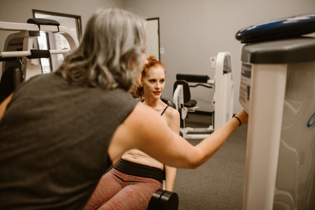 Two women engaging in a workout routine in a gym, focusing on fitness and strength.